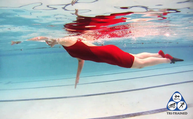 Underwater view of swimmer in red swimming costume performing doggy paddle swim drill